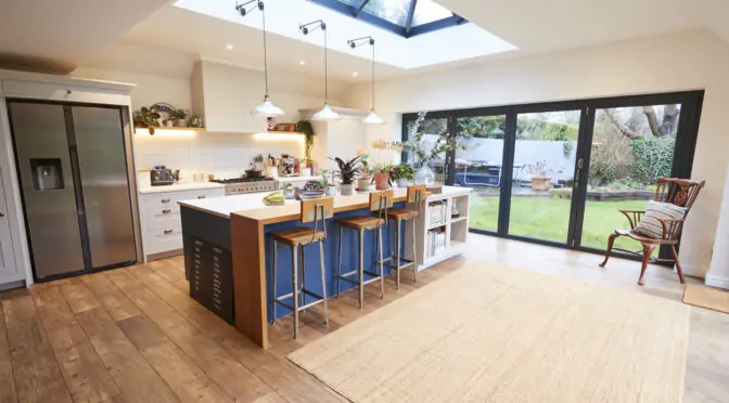 Open-plan kitchen with skylight, bi-fold doors, wooden floor, island seating, and garden view.